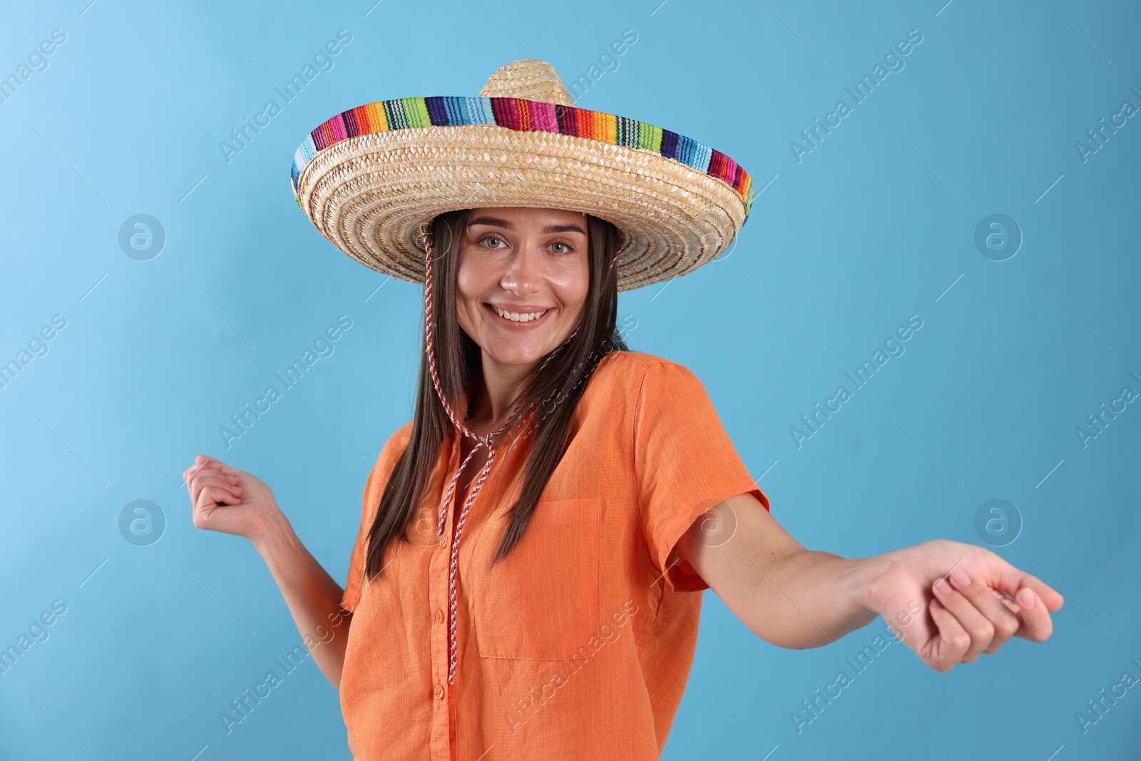 Happy woman in sombrero hat dancing on light blue background Photo of Happy woman in sombrero hat dancing on light blue background