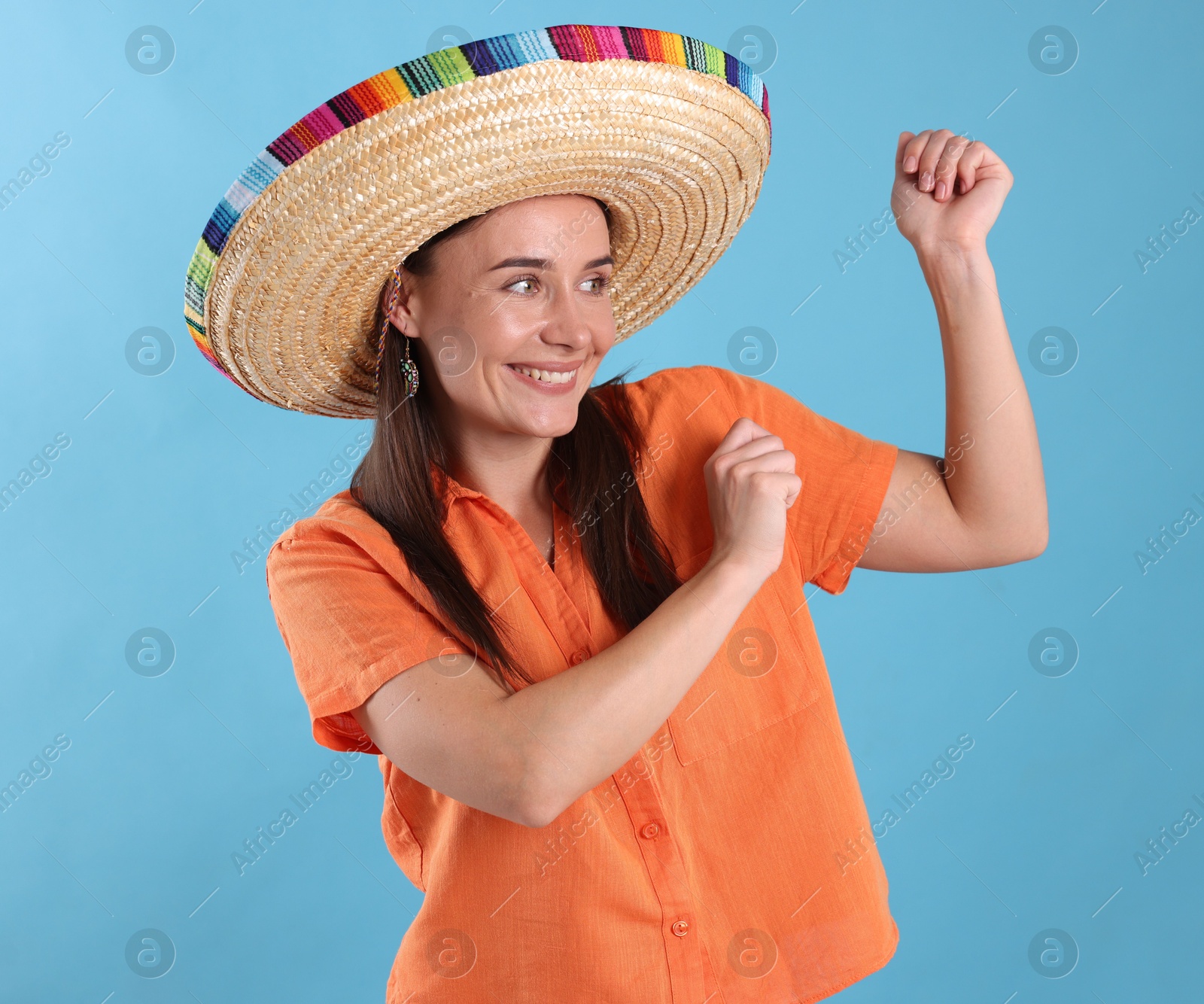 Happy woman in sombrero hat dancing on light blue background Photo of Happy woman in sombrero hat dancing on light blue background