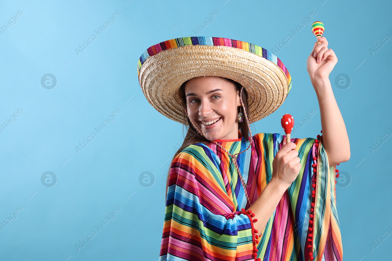 Happy woman in sombrero hat and colorful poncho playing maracas on light blue background. Space for text Photo of Happy woman in sombrero hat and colorful poncho playing maracas on light blue background. Space for text
