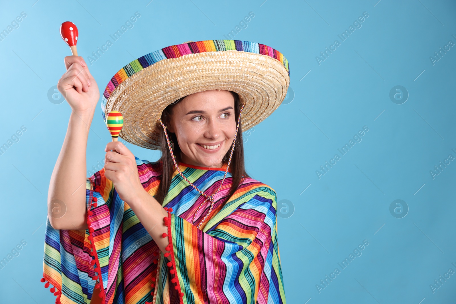 Happy woman in sombrero hat and colorful poncho playing maracas on light blue background. Space for text Photo of Happy woman in sombrero hat and colorful poncho playing maracas on light blue background. Space for text