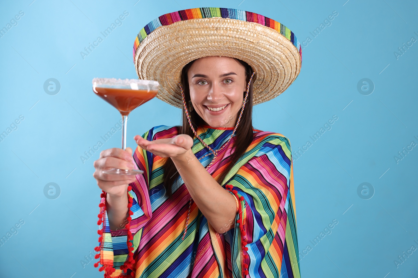 Smiling woman in sombrero hat with cocktail on light blue background Photo of Smiling woman in sombrero hat with cocktail on light blue background