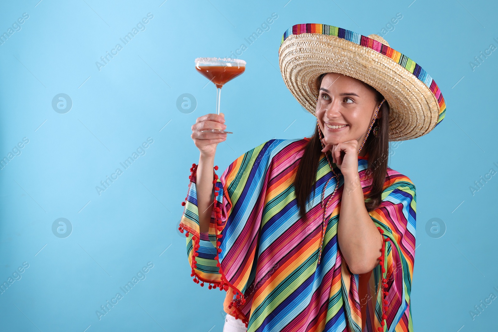 Smiling woman in sombrero hat with cocktail on light blue background. Space for text Photo of Smiling woman in sombrero hat with cocktail on light blue background. Space for text