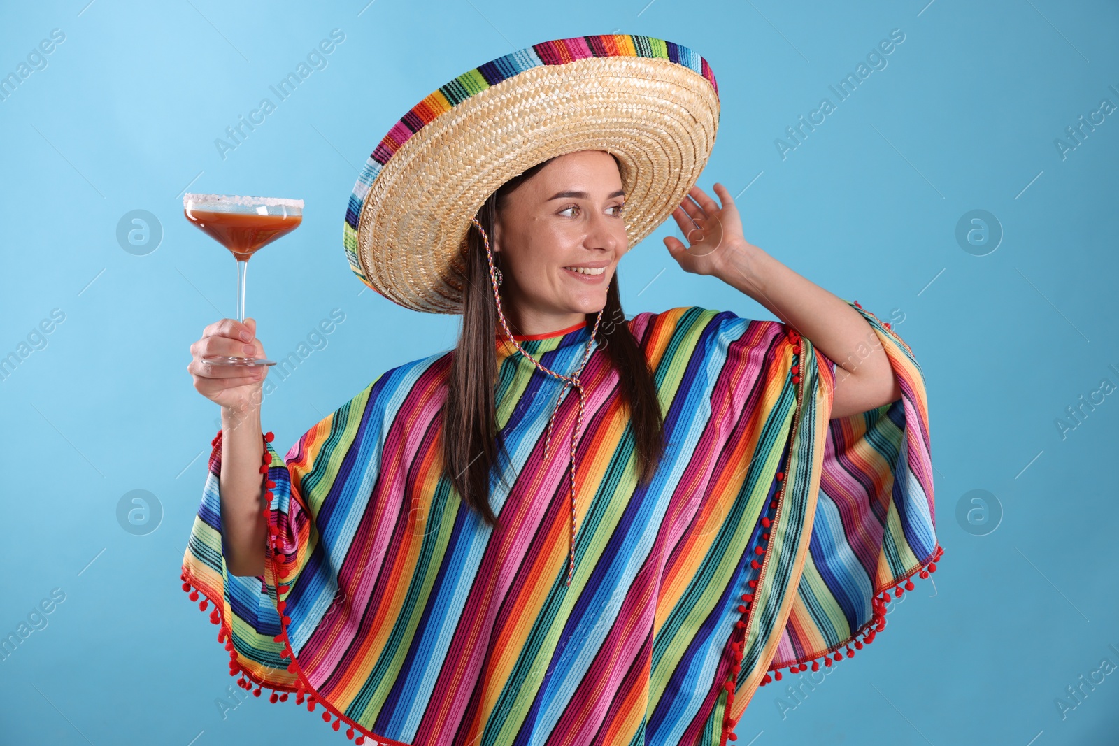 Smiling woman in sombrero hat with cocktail on light blue background Photo of Smiling woman in sombrero hat with cocktail on light blue background