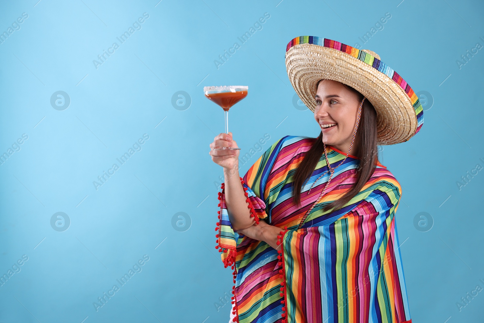 Smiling woman in sombrero hat with cocktail on light blue background. Space for text Photo of Smiling woman in sombrero hat with cocktail on light blue background. Space for text