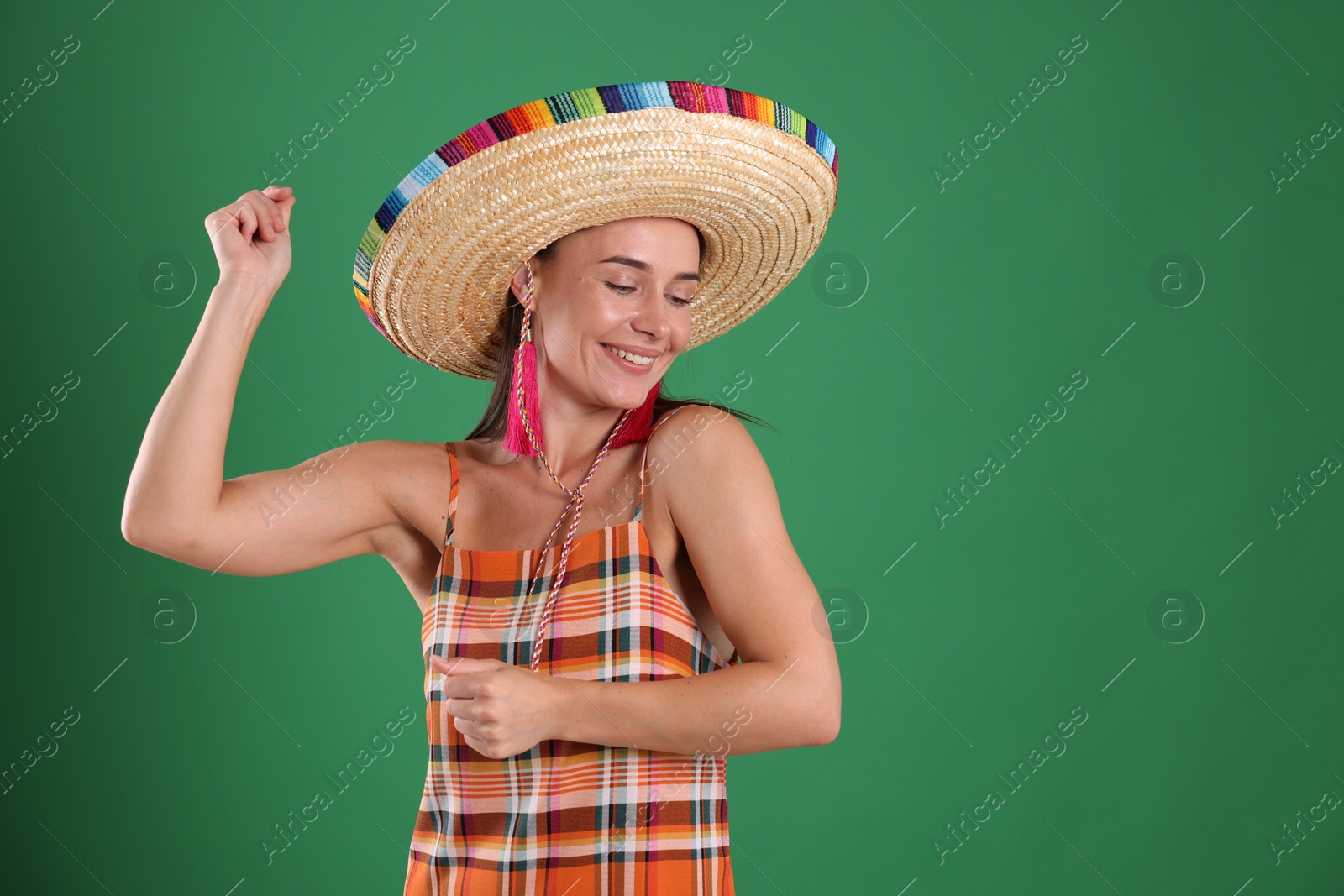 Smiling woman in sombrero hat dancing on green background. Space for text Photo of Smiling woman in sombrero hat dancing on green background. Space for text