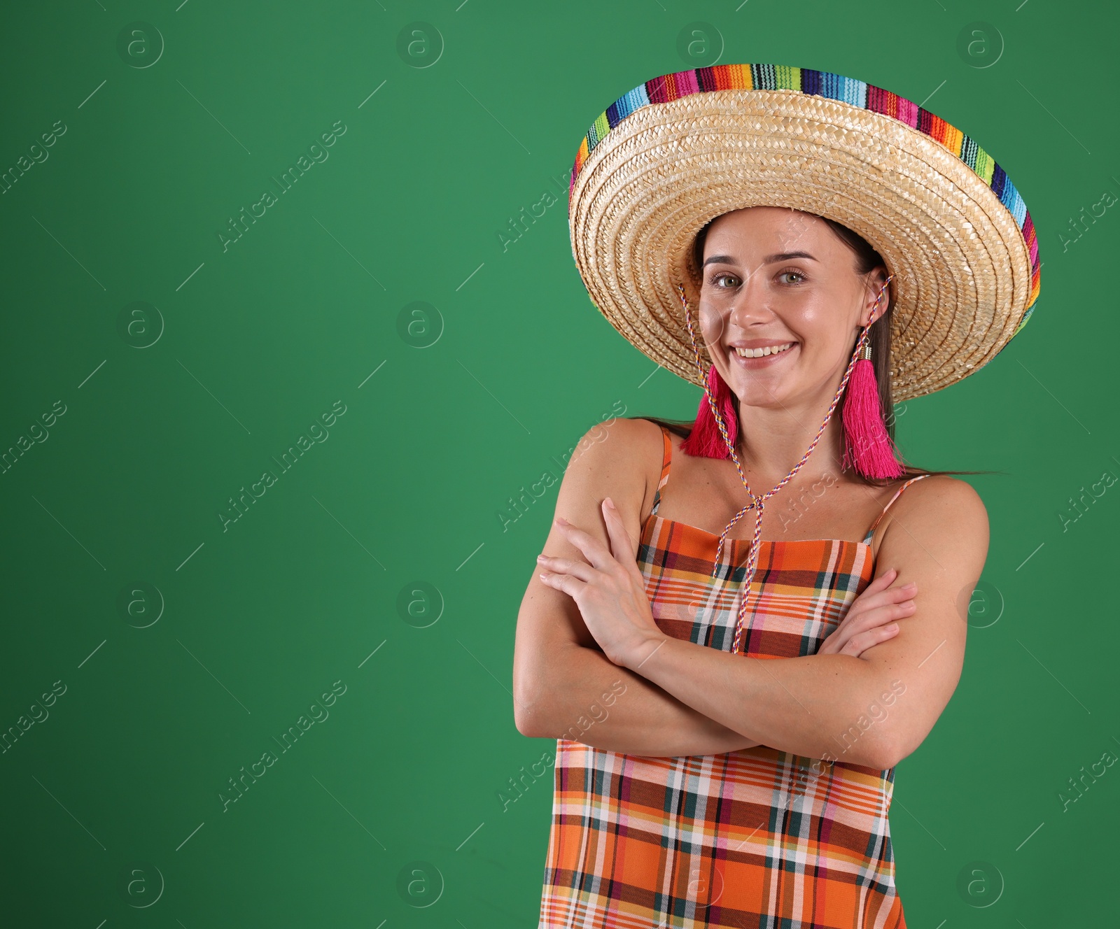 Smiling woman in sombrero hat with crossed arms on green background. Space for text Photo of Smiling woman in sombrero hat with crossed arms on green background. Space for text