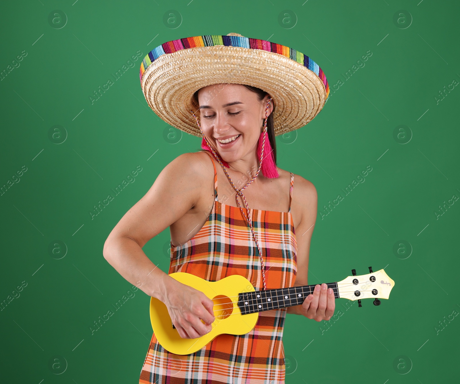 Smiling woman in sombrero hat playing ukulele on green background Photo of Smiling woman in sombrero hat playing ukulele on green background