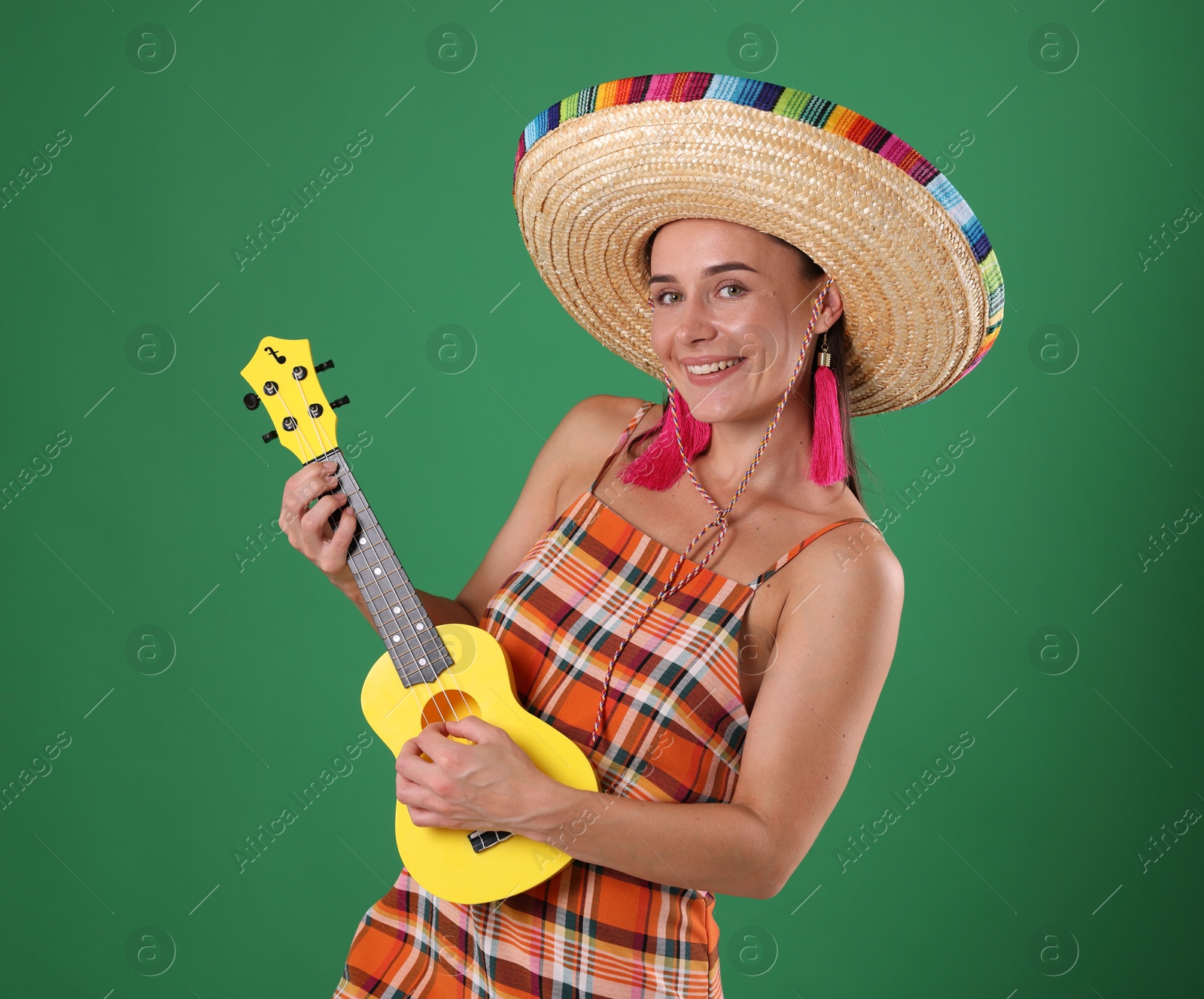 Smiling woman in sombrero hat playing ukulele on green background Photo of Smiling woman in sombrero hat playing ukulele on green background