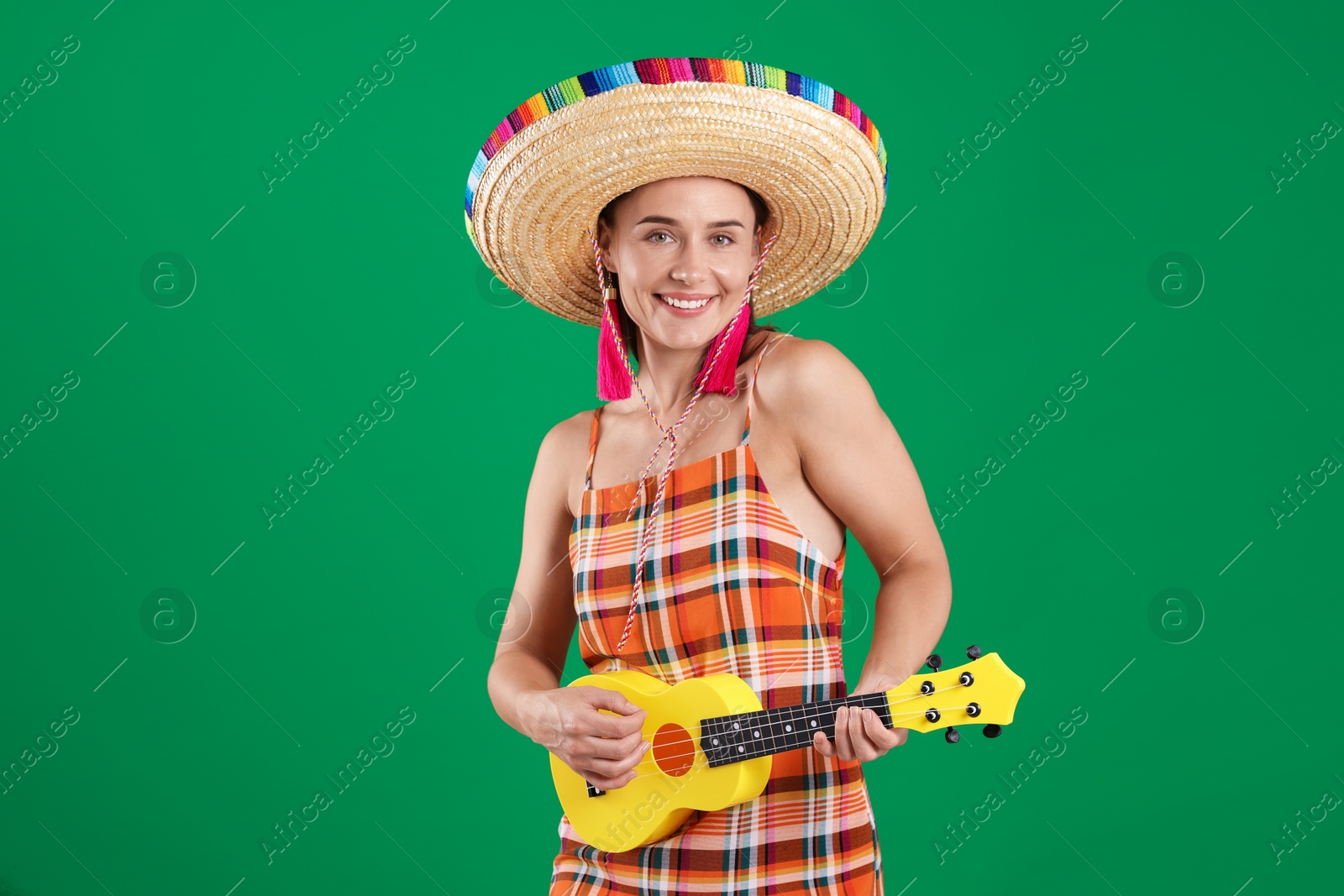 Smiling woman in sombrero hat playing ukulele on green background Photo of Smiling woman in sombrero hat playing ukulele on green background