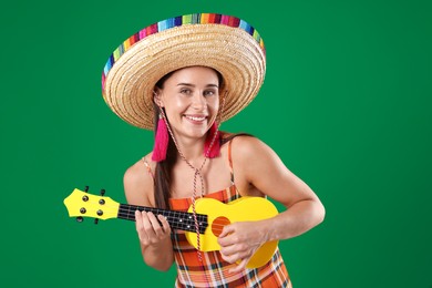 Photo of Smiling woman in sombrero hat playing ukulele on green background