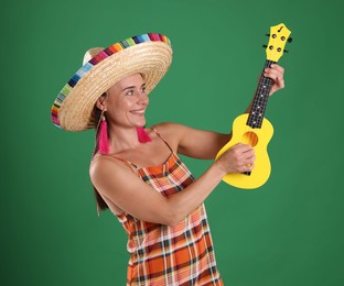 Photo of Smiling woman in sombrero hat playing ukulele on green background