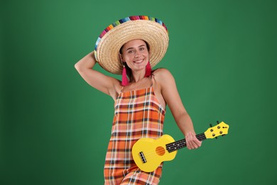Photo of Smiling woman in sombrero hat with ukulele on green background