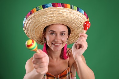 Photo of Smiling woman in sombrero hat playing maracas on green background