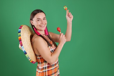 Photo of Smiling woman with sombrero hat playing maracas on green background. Space for text