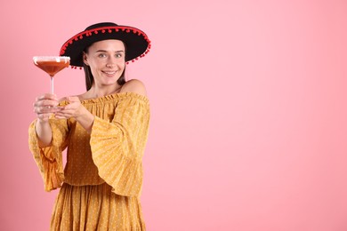 Photo of Smiling woman in black Flamenco hat and dress with cocktail on pink background. Space for text
