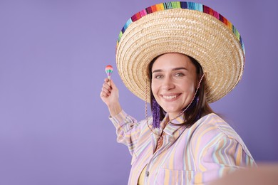 Photo of Smiling woman in sombrero hat and maracas taking selfie on violet background. Space for text