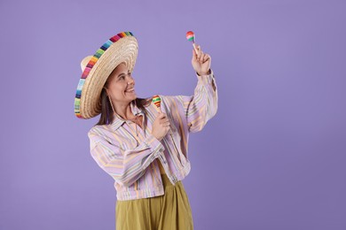 Photo of Smiling woman in sombrero hat playing maracas on violet background