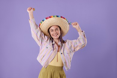 Photo of Smiling woman in sombrero hat playing maracas on violet background