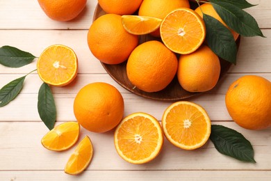 Photo of Fresh ripe oranges and leaves on light wooden table, flat lay