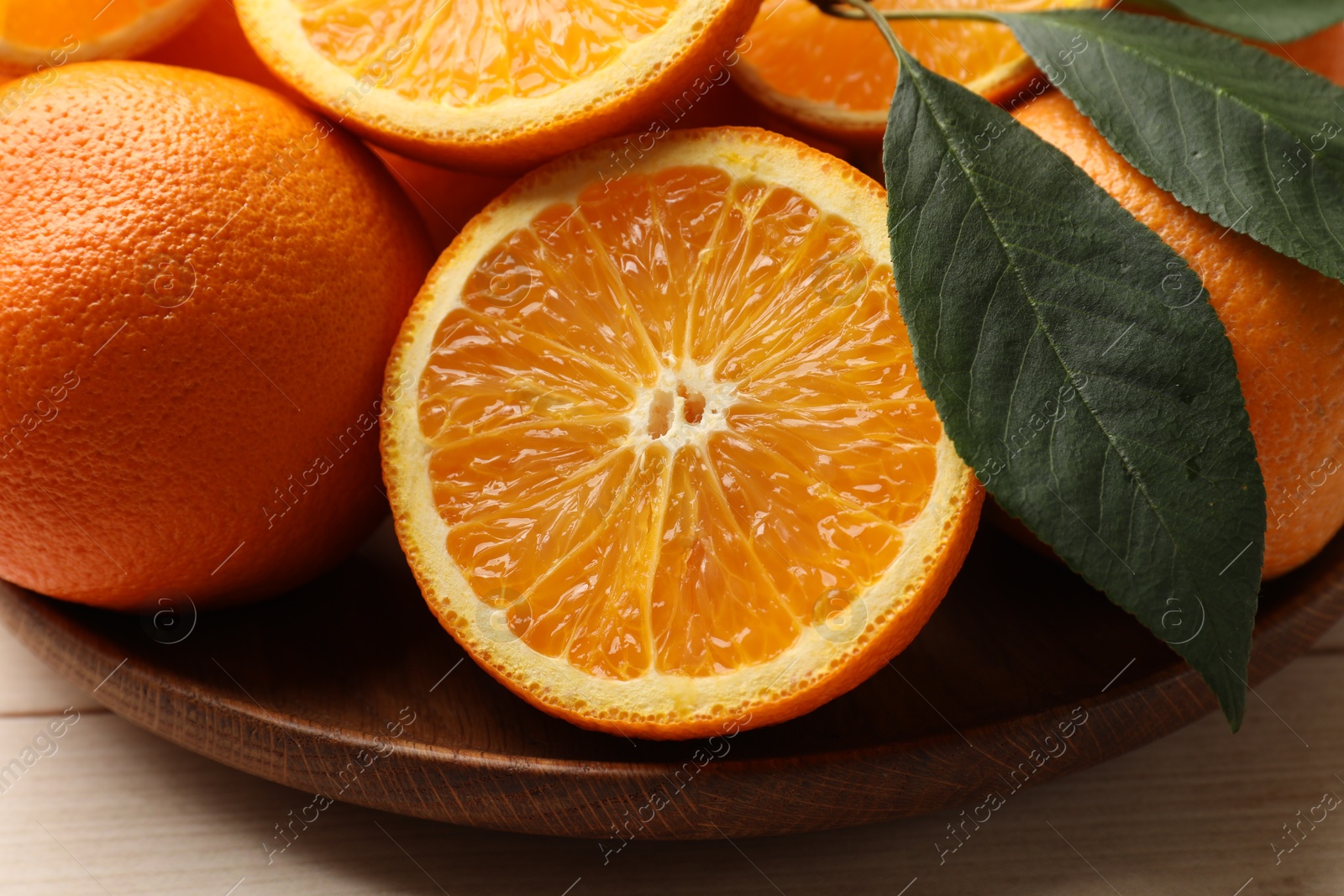 Fresh ripe oranges and leaves on light wooden table, closeup Photo of Fresh ripe oranges and leaves on light wooden table, closeup
