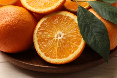 Photo of Fresh ripe oranges and leaves on light wooden table, closeup