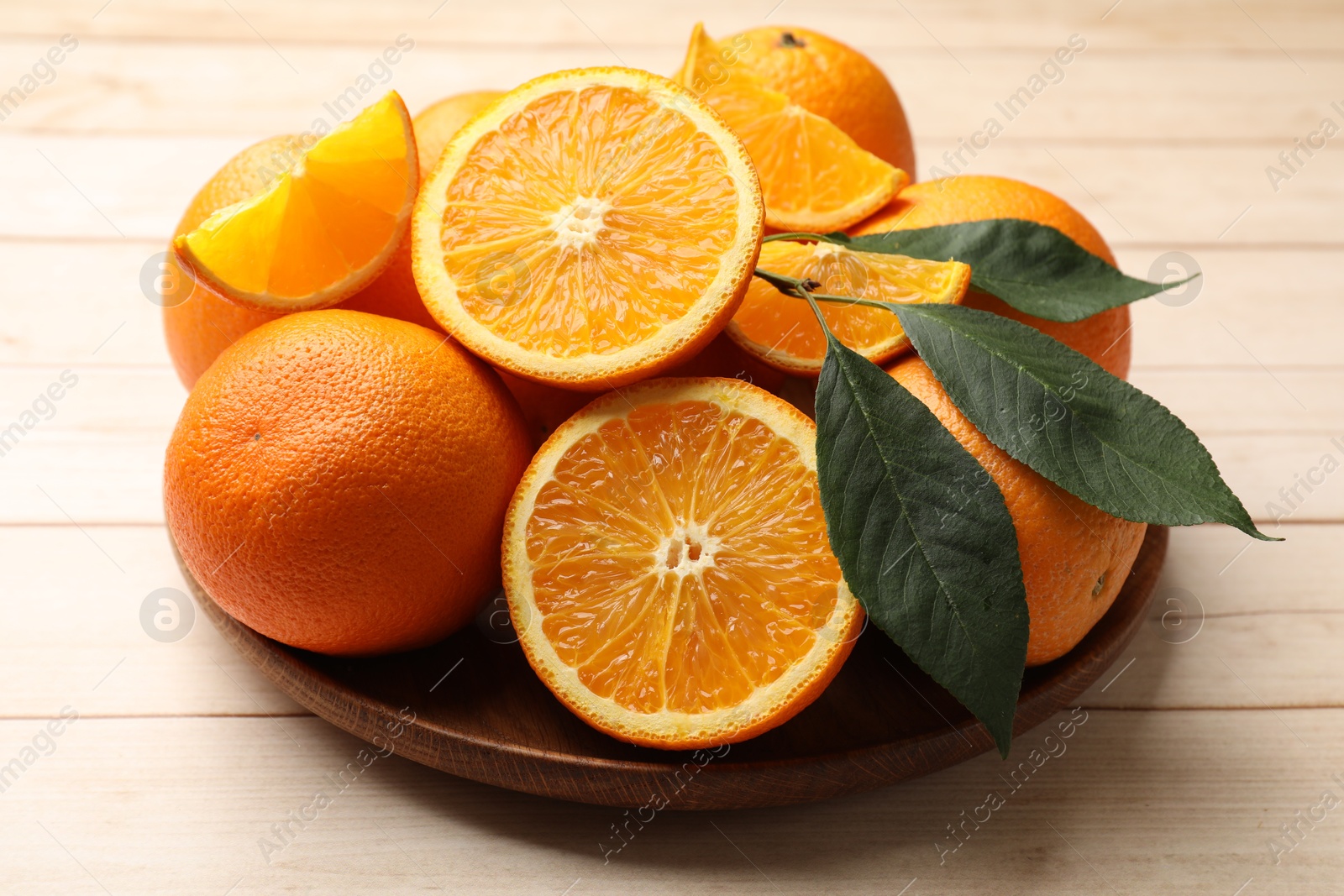 Fresh ripe oranges and leaves on light wooden table, closeup Photo of Fresh ripe oranges and leaves on light wooden table, closeup