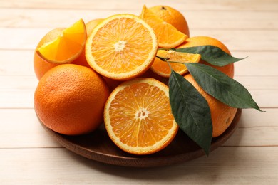Photo of Fresh ripe oranges and leaves on light wooden table, closeup