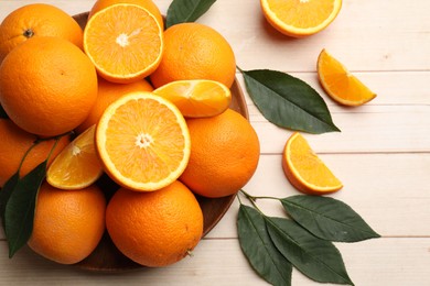 Photo of Fresh ripe oranges and leaves on light wooden table, flat lay