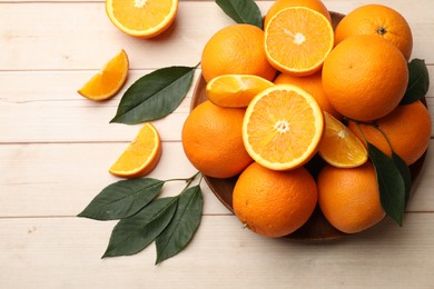 Photo of Fresh ripe oranges and leaves on light wooden table, flat lay