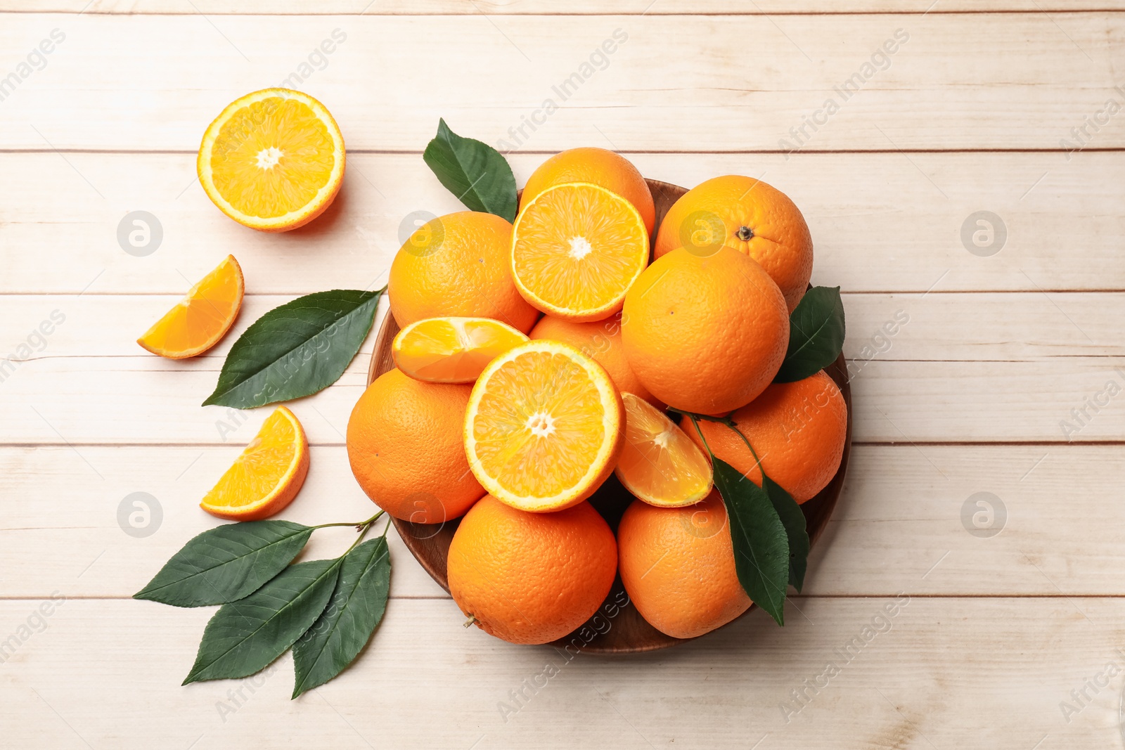 Fresh ripe oranges and leaves on light wooden table, flat lay. Space for text Photo of Fresh ripe oranges and leaves on light wooden table, flat lay. Space for text