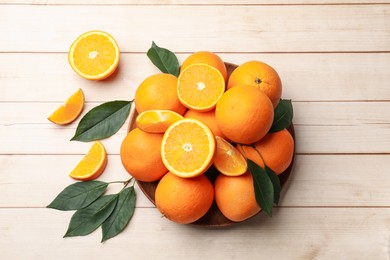 Photo of Fresh ripe oranges and leaves on light wooden table, flat lay. Space for text