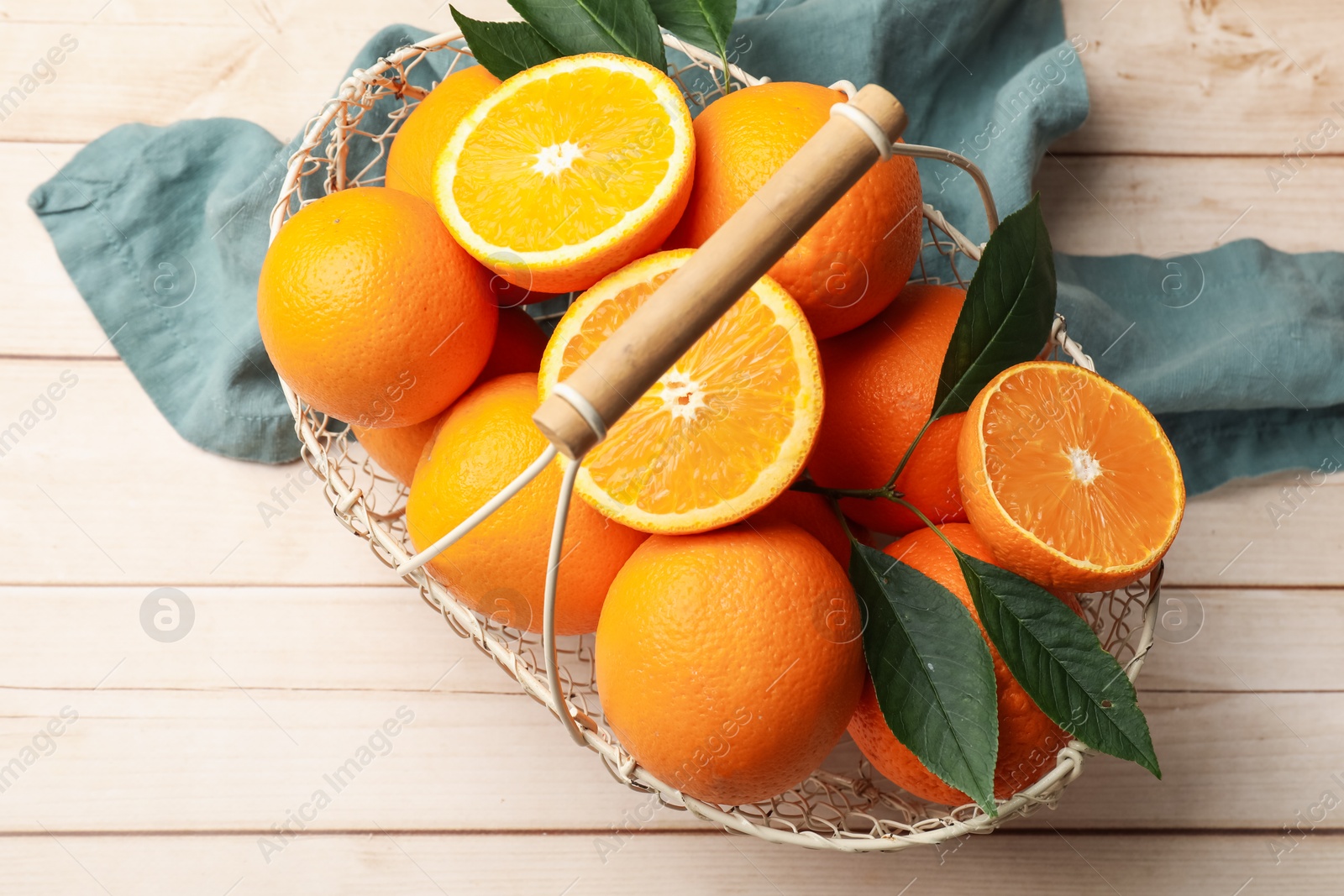 Photo of Fresh ripe oranges and leaves in basket on light wooden table, top view