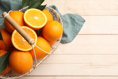 Photo of Fresh ripe oranges and leaves in basket on light wooden table, top view. Space for text