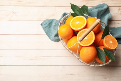 Photo of Fresh ripe oranges and leaves in basket on light wooden table, top view. Space for text