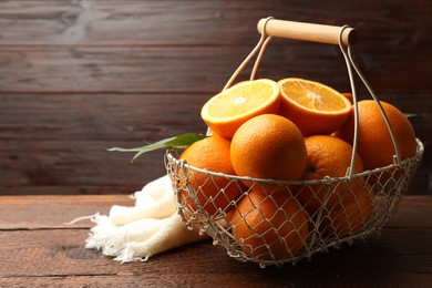 Photo of Fresh ripe oranges and leaves in basket on wooden table, closeup. Space for text