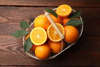 Photo of Fresh ripe oranges and leaves in basket on wooden table, top view