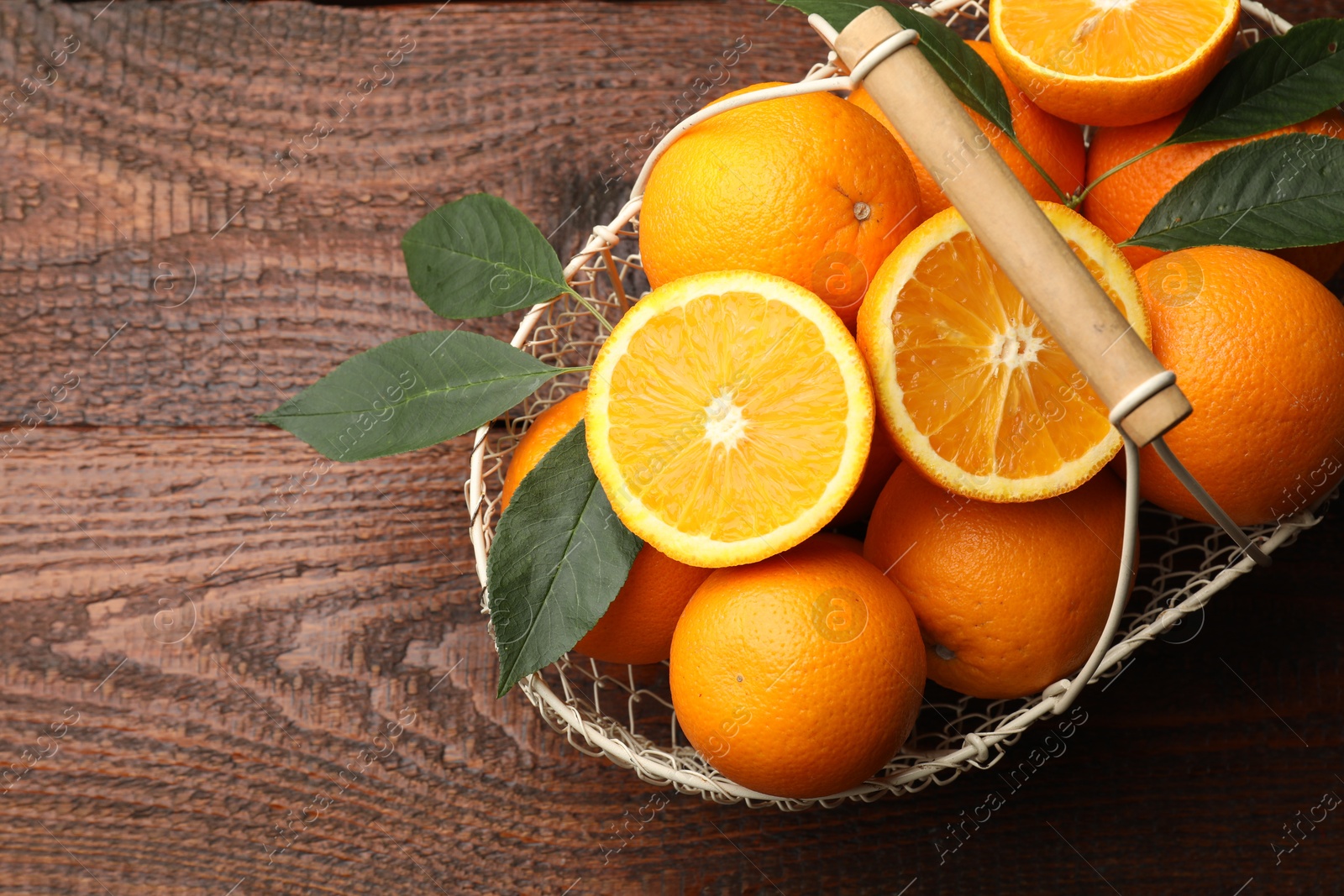 Fresh ripe oranges and leaves in basket on wooden table, top view. Space for text Photo of Fresh ripe oranges and leaves in basket on wooden table, top view. Space for text