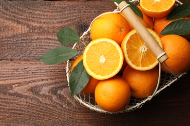 Photo of Fresh ripe oranges and leaves in basket on wooden table, top view. Space for text