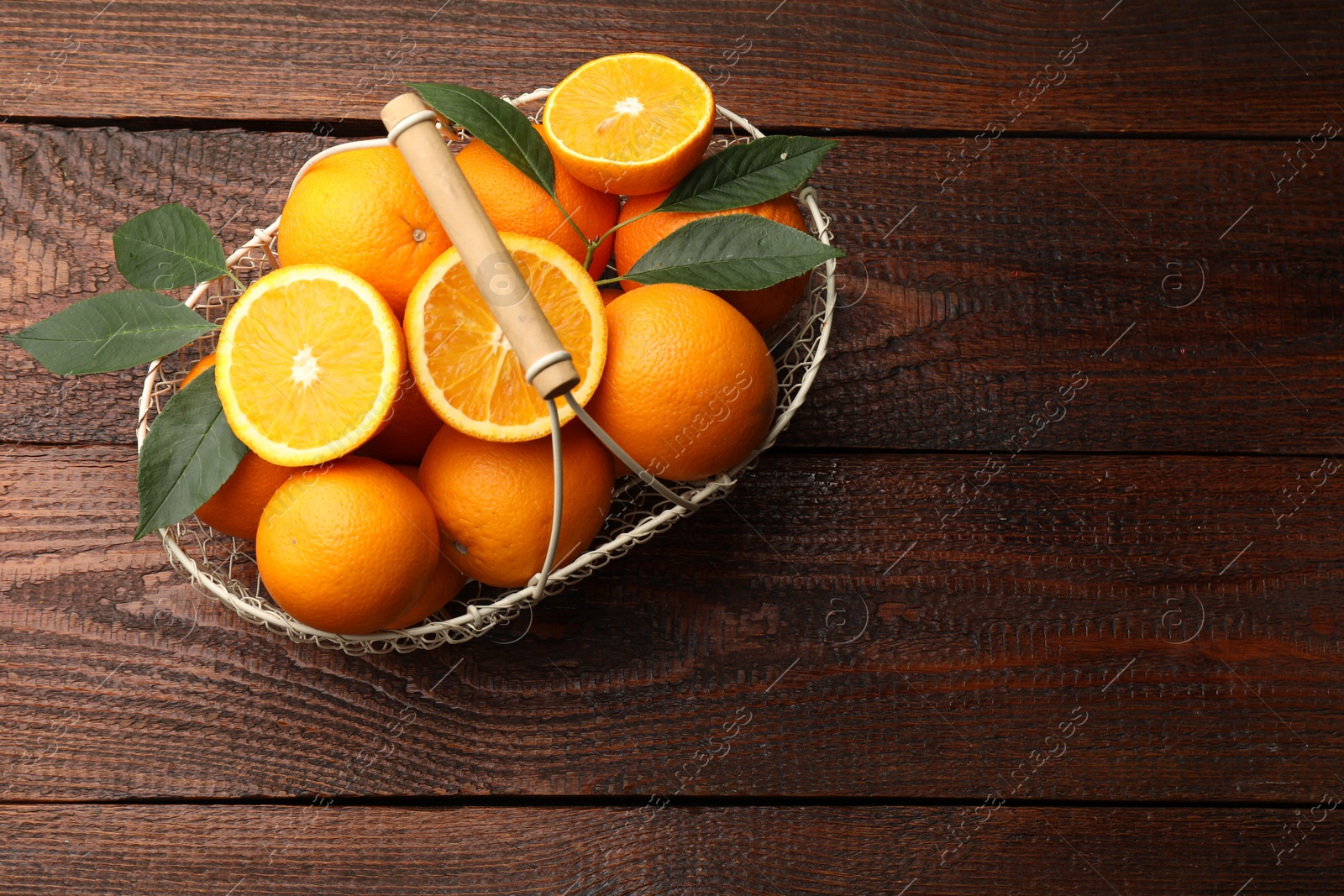 Fresh ripe oranges and leaves in basket on wooden table, top view. Space for text Photo of Fresh ripe oranges and leaves in basket on wooden table, top view. Space for text