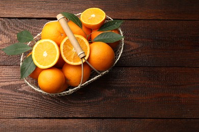 Photo of Fresh ripe oranges and leaves in basket on wooden table, top view. Space for text