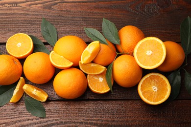 Photo of Fresh ripe oranges and leaves on wooden table, flat lay