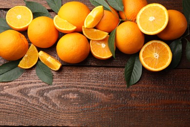 Photo of Fresh ripe oranges and leaves on wooden table, flat lay. Space for text