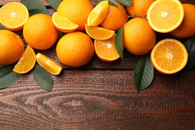 Photo of Fresh ripe oranges and leaves on wooden table, flat lay. Space for text