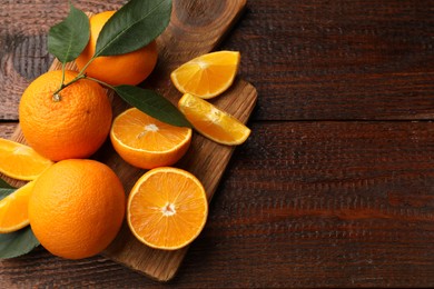 Photo of Fresh ripe oranges and leaves on wooden table, top view. Space for text