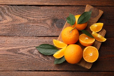 Photo of Fresh ripe oranges and leaves on wooden table, top view. Space for text