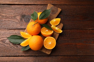 Photo of Fresh ripe oranges and leaves on wooden table, top view. Space for text