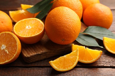 Photo of Fresh ripe oranges and leaves on wooden table, closeup