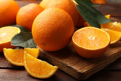 Photo of Fresh ripe oranges and leaves on wooden table, closeup