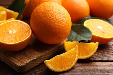 Photo of Fresh ripe oranges and leaves on wooden table, closeup