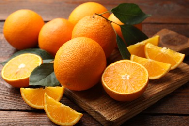 Photo of Fresh ripe oranges and leaves on wooden table, closeup